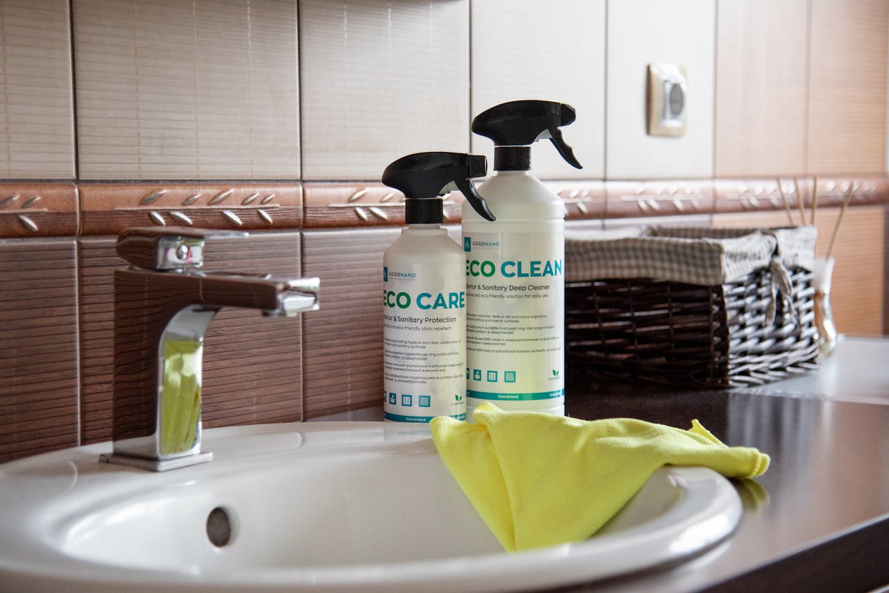 hero-img-01 Eco-friendly cleaning products displayed on a bathroom sink with tiles and a basket.