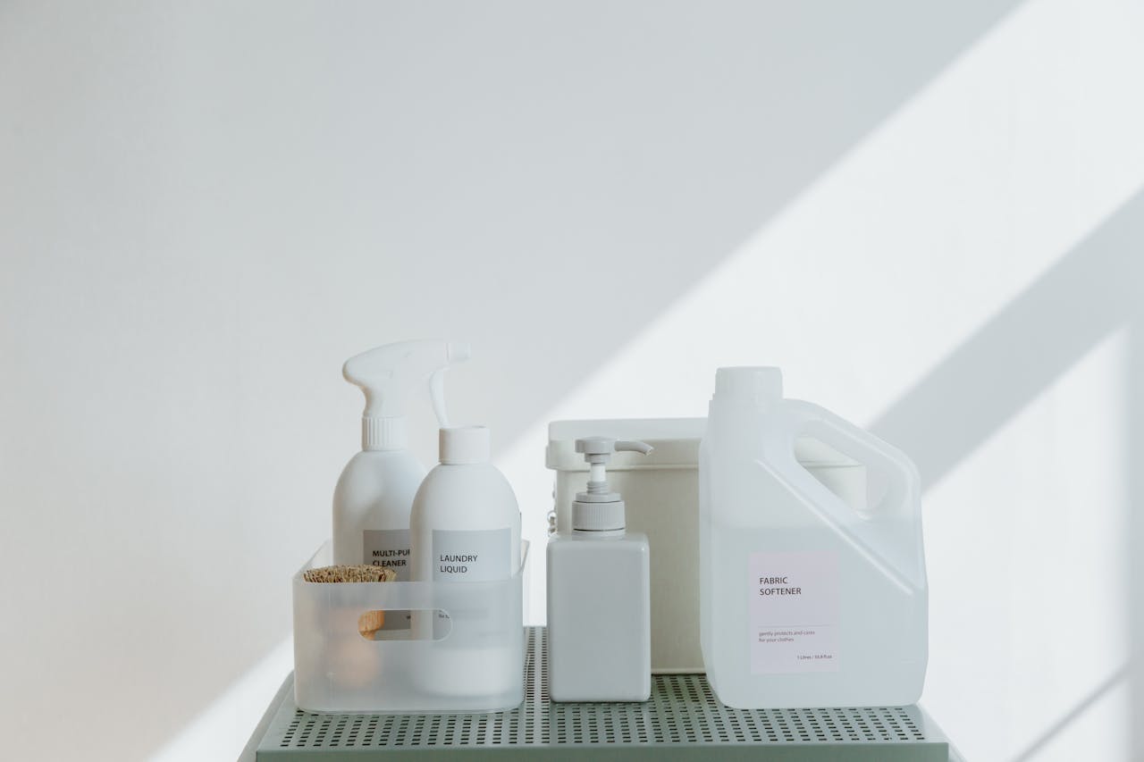hero-img-02 Clean and simple display of various cleaning products in soft lighting on a white background.